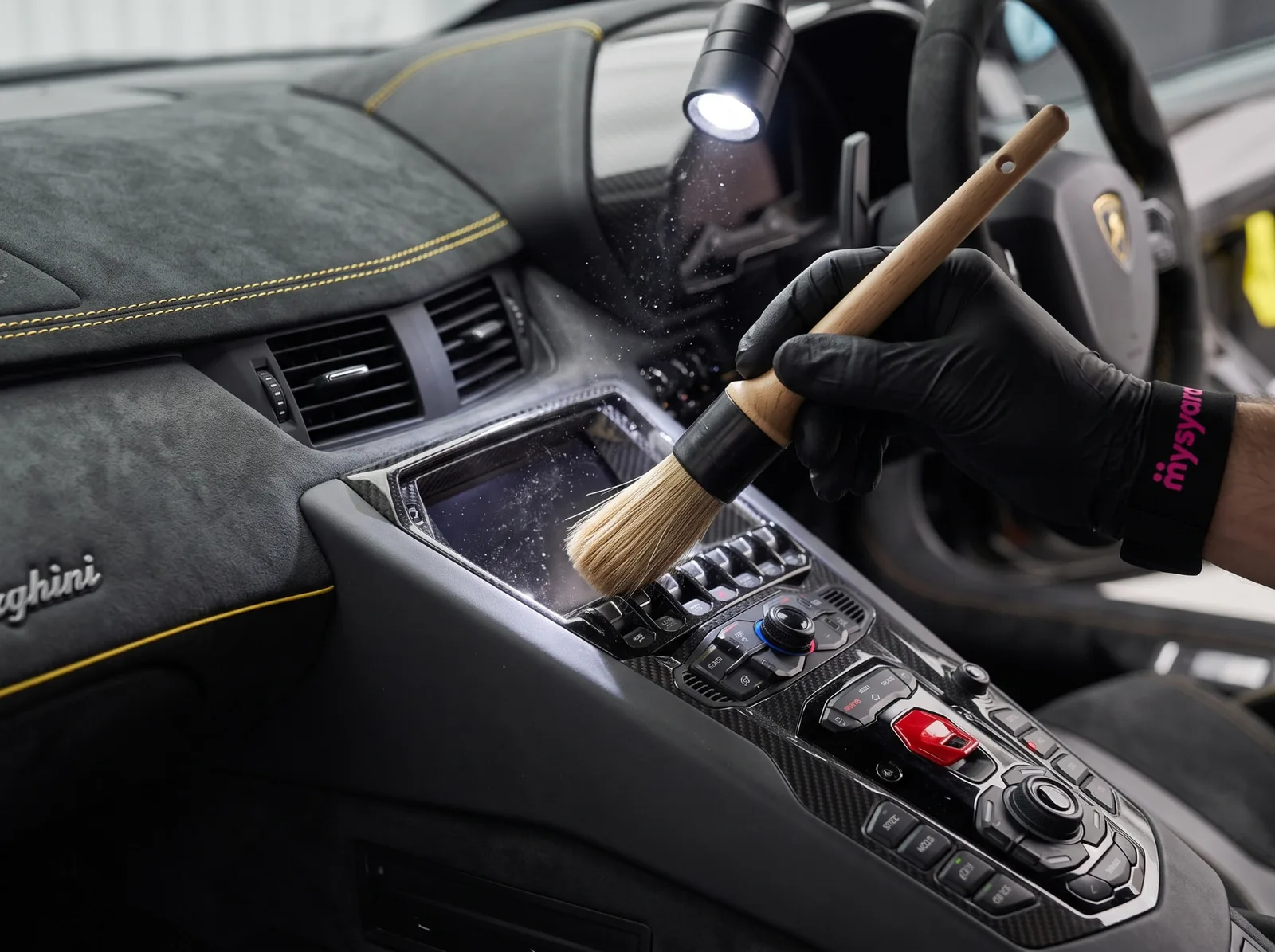 A gloved MySyara Pro dusting the centre console of a Lamborghini with a detailing brush